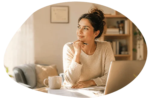 "Woman sitting at a desk with a laptop, resting her chin on her hand and smiling thoughtfully."