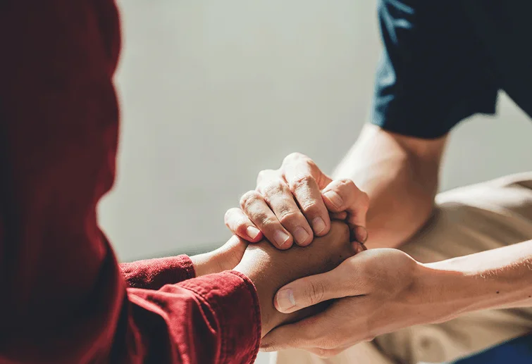 "Close-up of two people's hands clasped together in a comforting gesture."