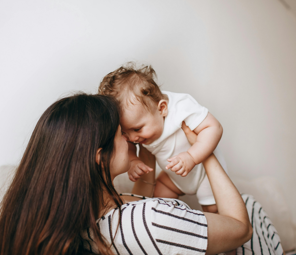 Mother lifting and smiling at her baby, foreheads close together.